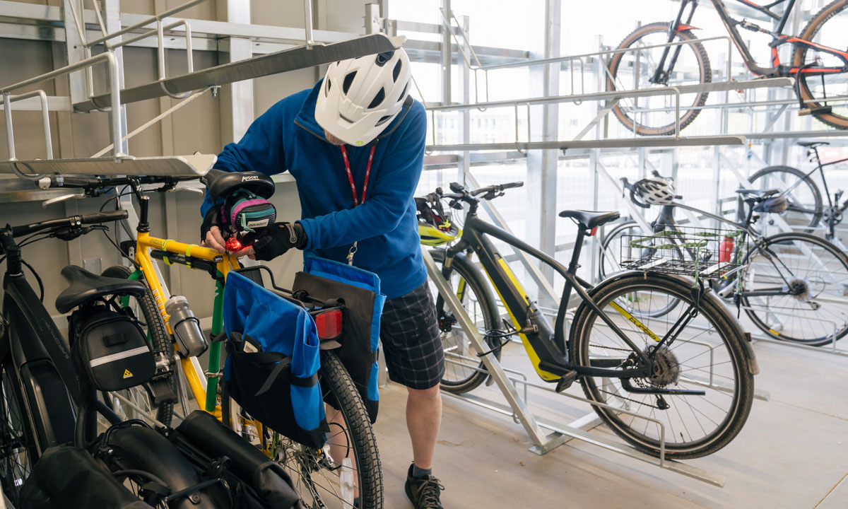 A person is locking is bike in the new bike storage facility. There are seven other bikes around him, one of which is on an upper rack.