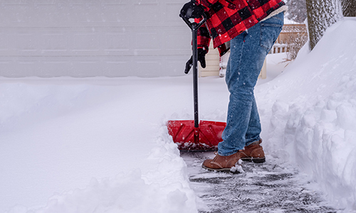 Person in a flannel coat shoveling snow off of a driveway