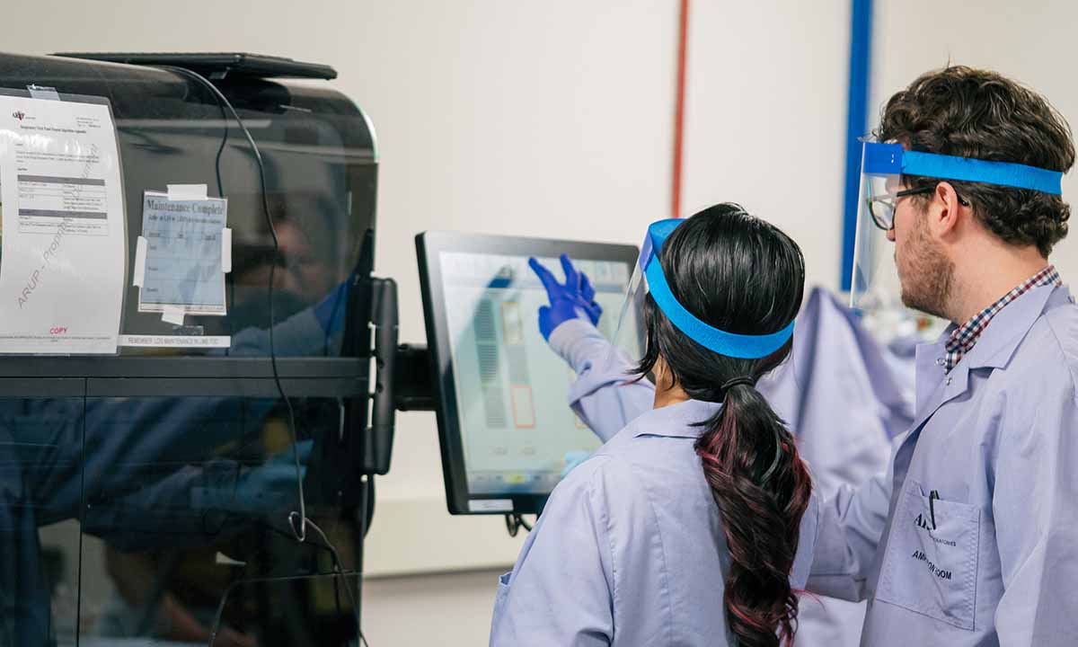 Two medical laboratory professionals observe a viewscreen on a machine.