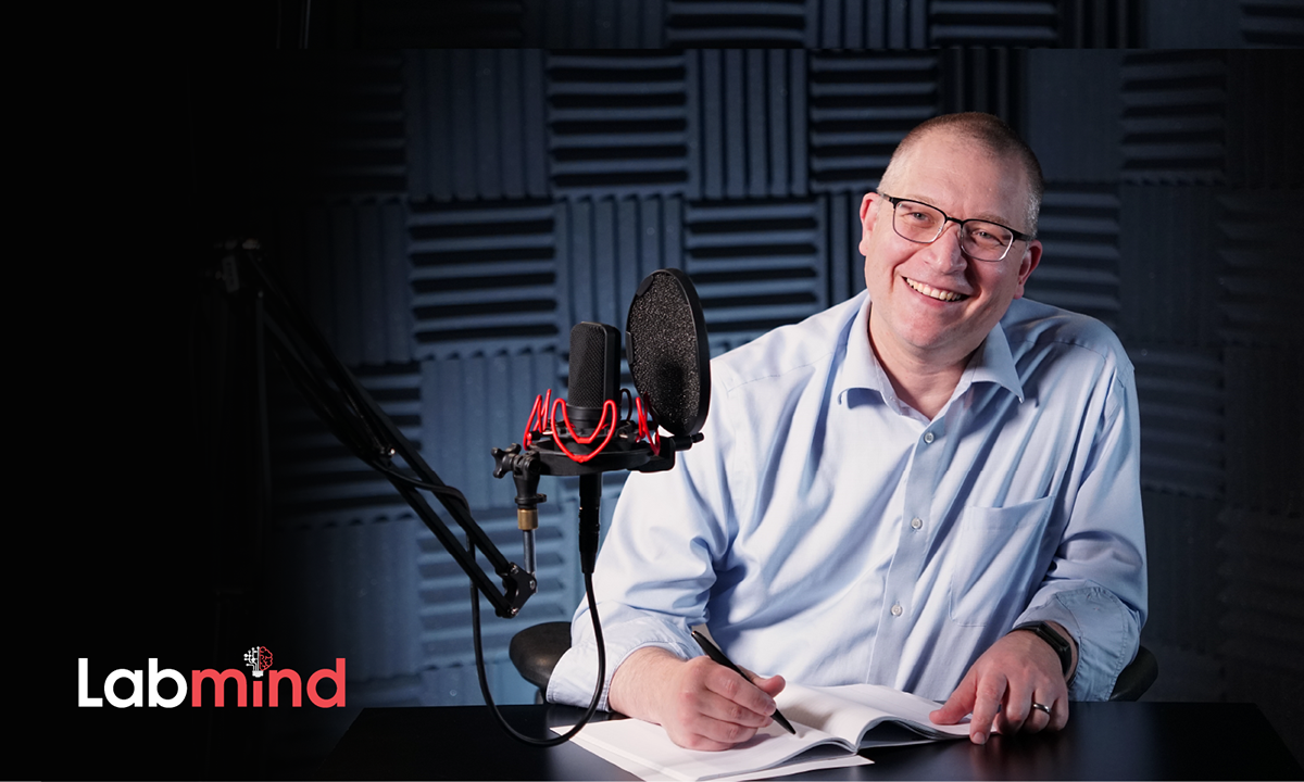 Jonathan Genzen smiles as he sits in front of a mic and writes in a notebook.