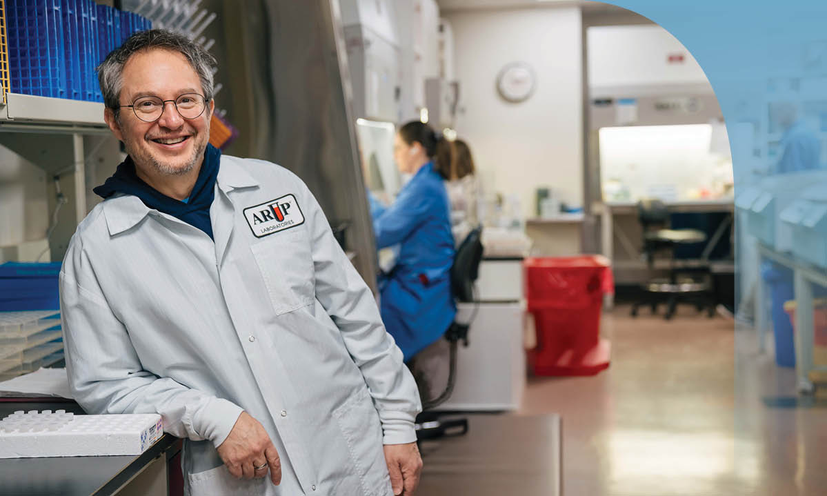 Adam Barker leans against a counter in a lab while smiling at the camera.