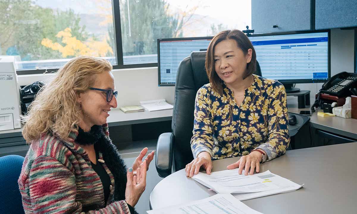 Pinar Bayrak-Toydemir and Rong Mao sit at a desk and talk.