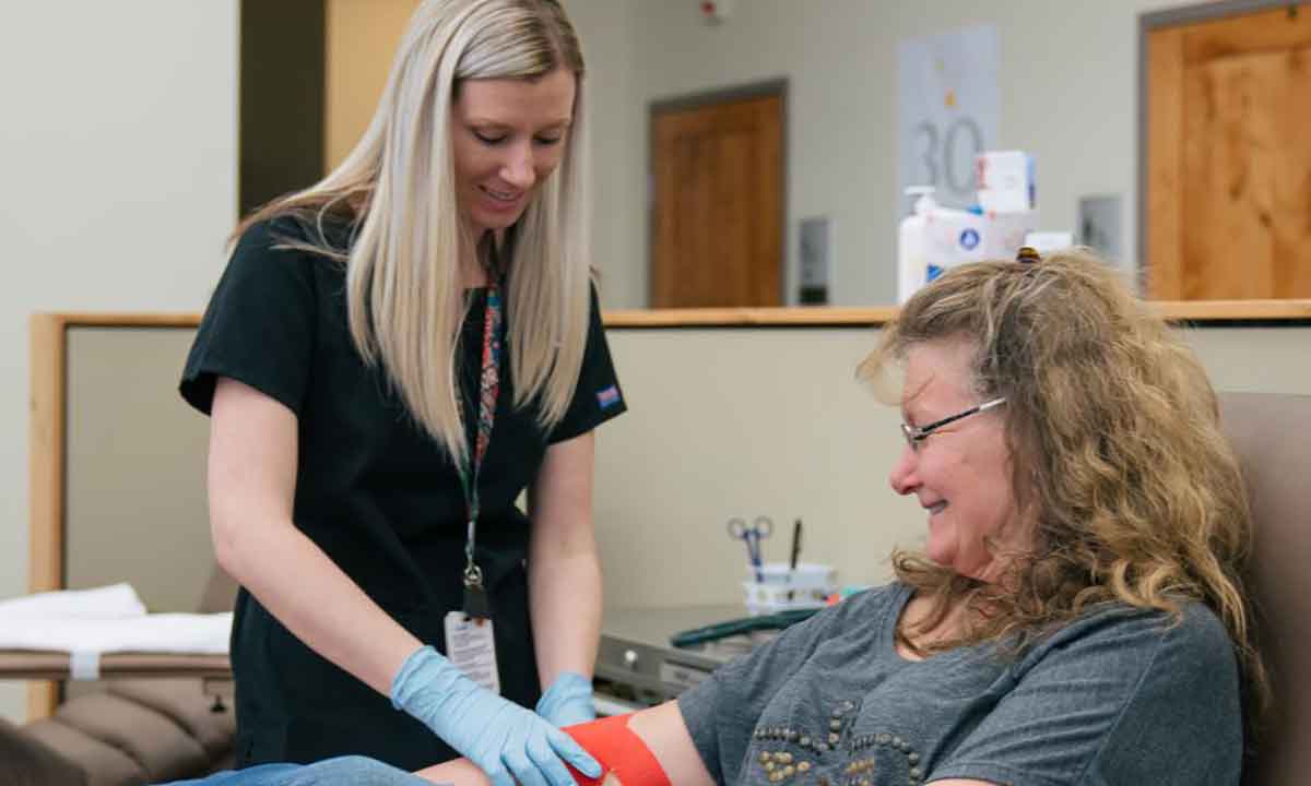 A woman who donated blood sits while another woman wraps the donor's arm.