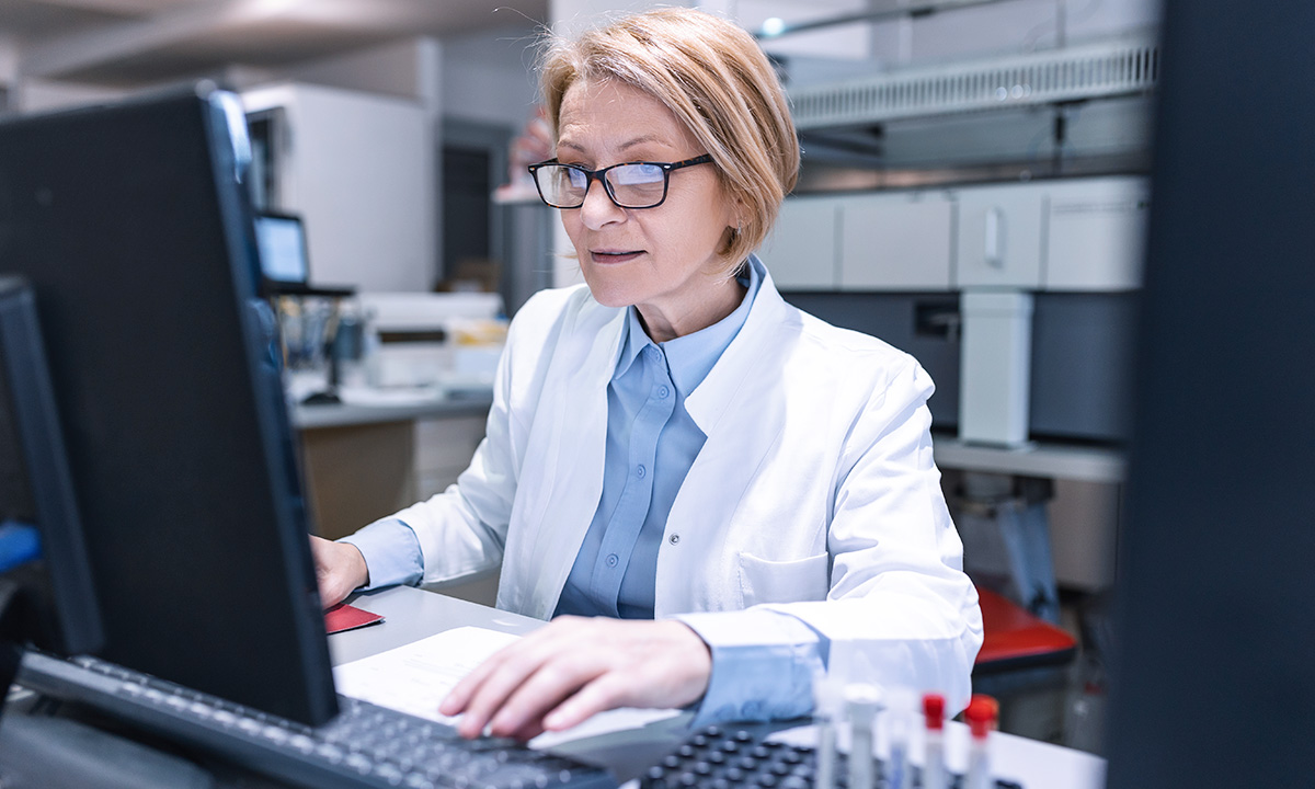 A woman in a lab coat works at a computer