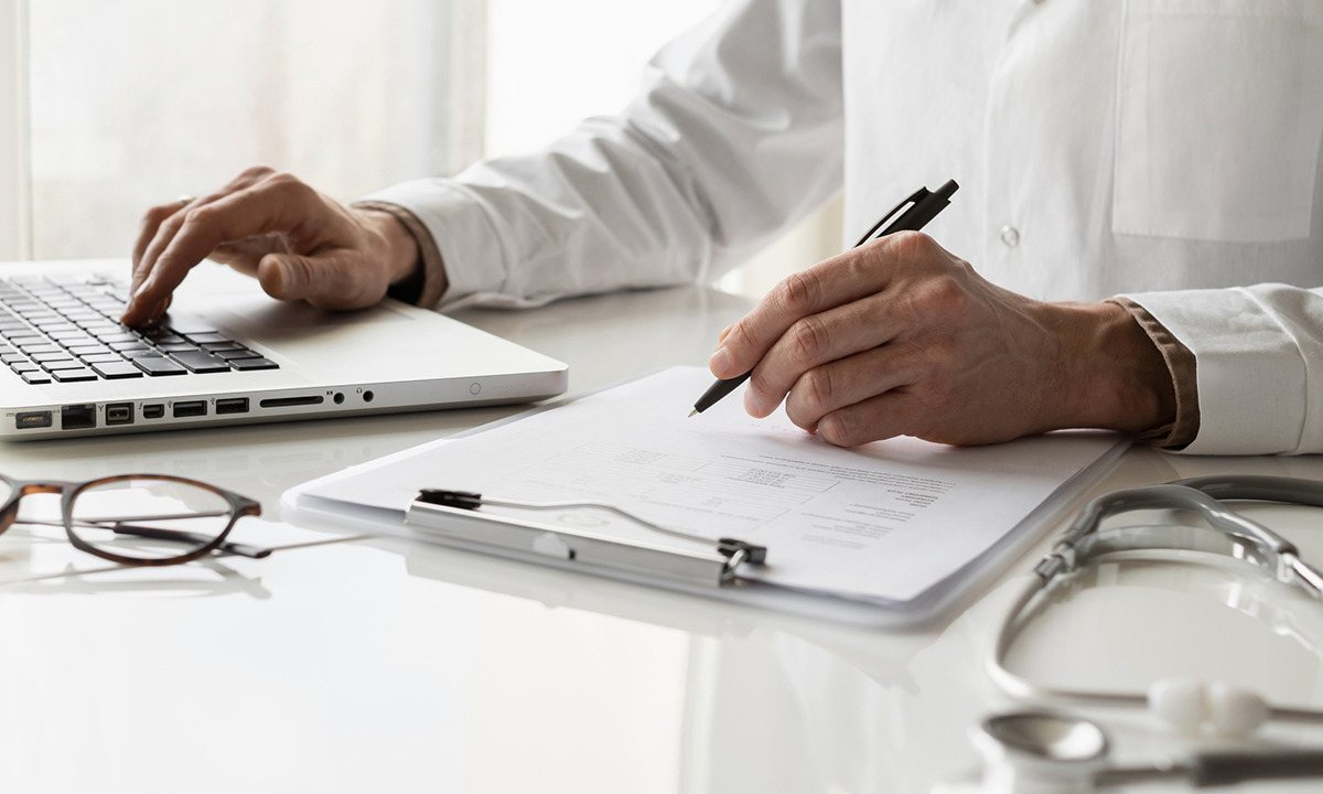 Clinician sits at desk, taking notes on papers attached to a clipboard.