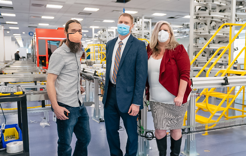 A group wearing masks stand in front of automated lab equipment