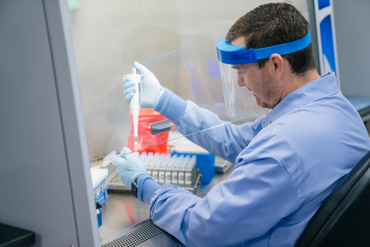 A lab technician works with a pipette and a tray of specimens