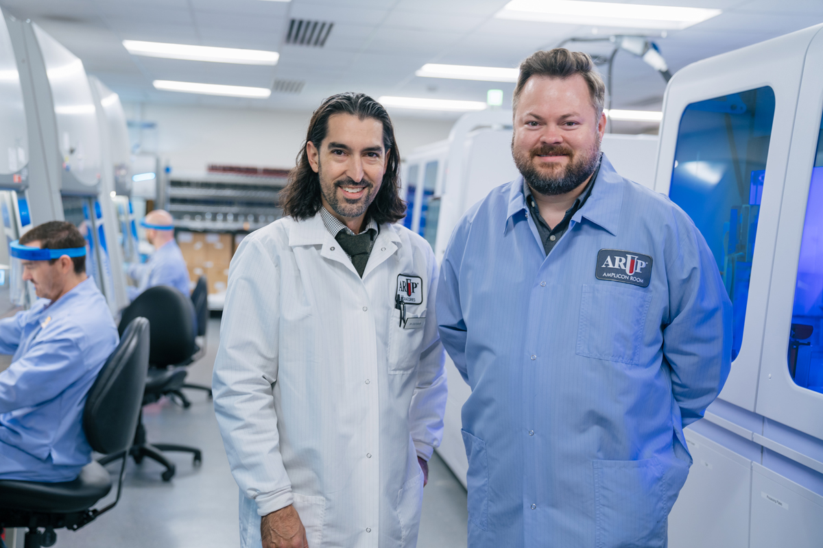 Two men in lab coats next to a large machine