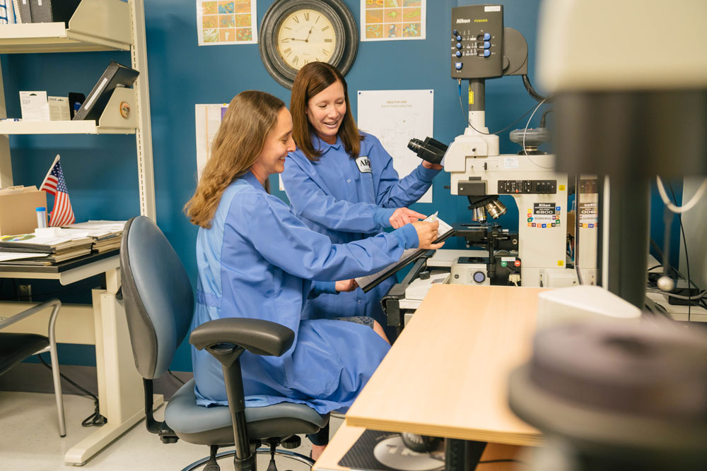 Tammy Smith and Lisa Peterson have a discussion at a microscope