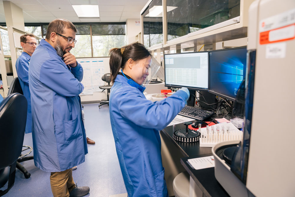 A woman and two men work on a test sample in a lab