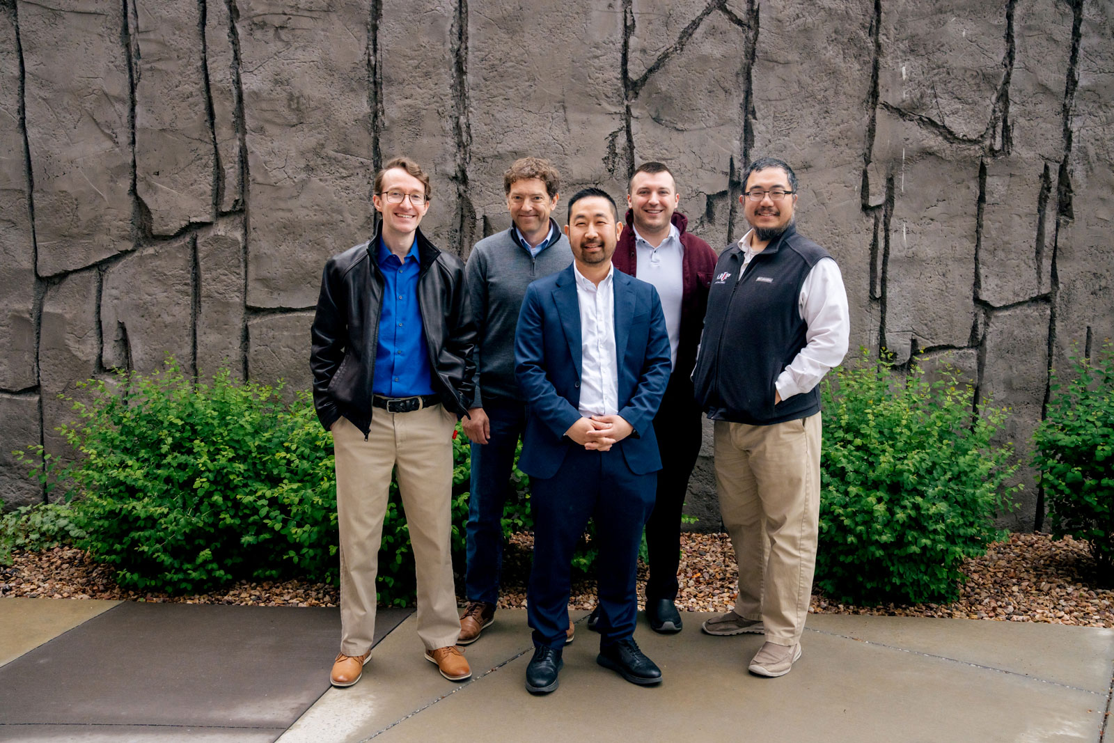 A group of people standing in front of an outside wall